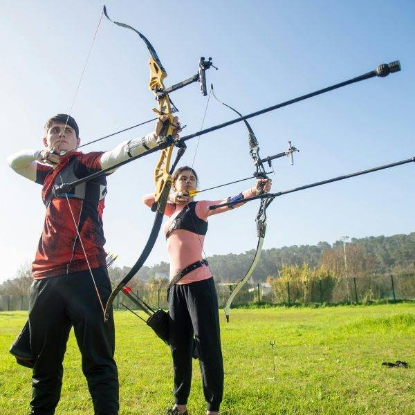 Teenage archers target practice in a sunny outdoor field in Portugal.