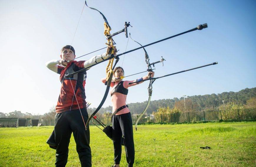 Teenage archers target practice in a sunny outdoor field in Portugal.